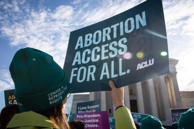 Person holds up ACLU sign that reads "Abortion Access for All" in front of the Supreme Court building.