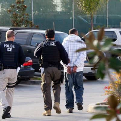Two Immigration and Customs Enforcement (ICE) agents take a person into custody