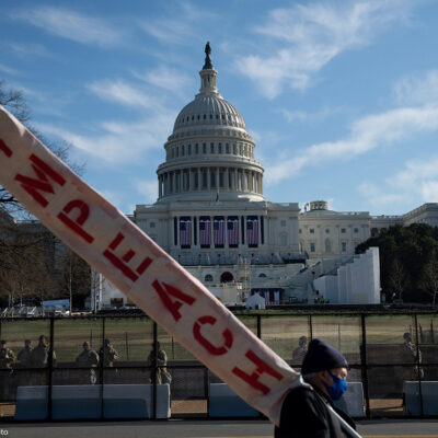 A man walks by the U.S. Capitol Building carrying a sign that reads "Impeach"
