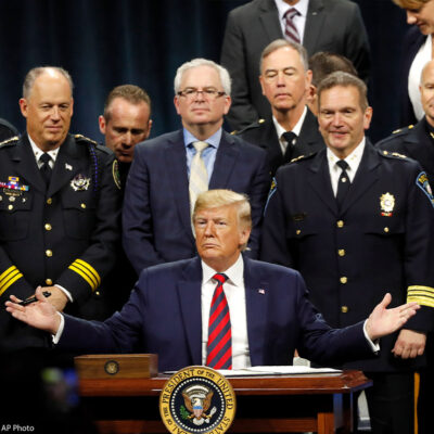 President Trump sits at podium ready to sign executive order creating a commission to study law enforcement and justice, surrounded by officers beside him in support.