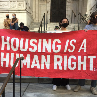 Protesters carrying a banner with the text "housing is a human right.