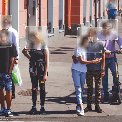 People standing at a crosswalk with face recognition software boxes superimposed over their faces.