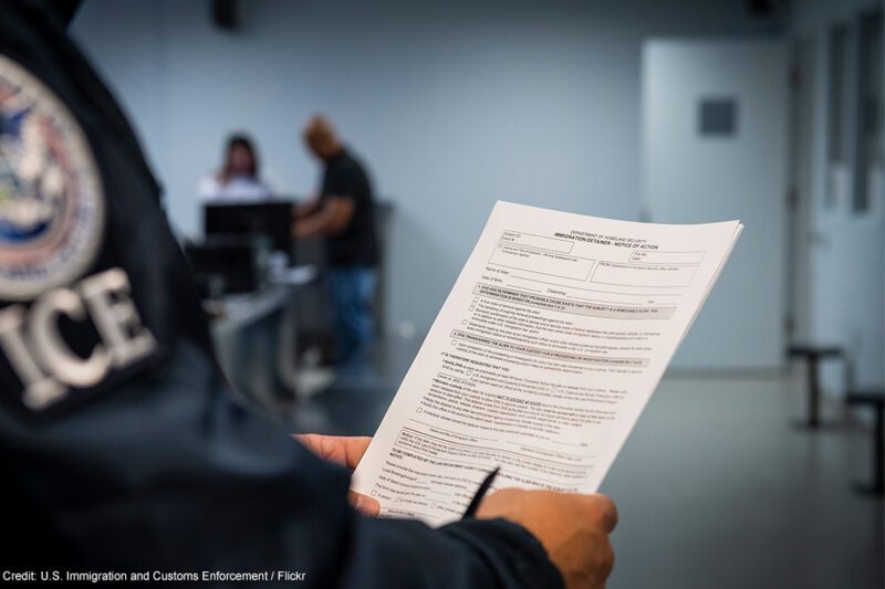 An ICE agent holding an Immigration Detainer form.
