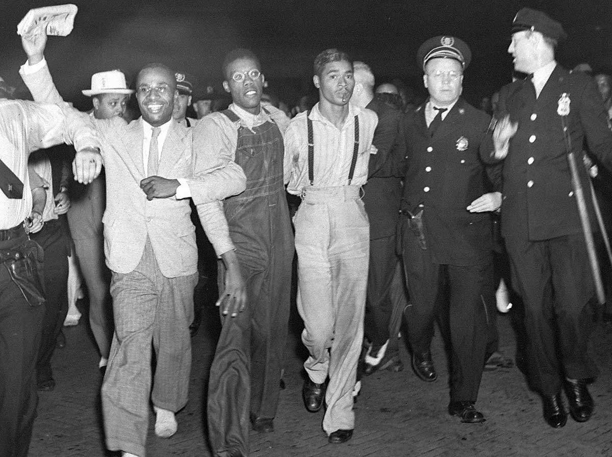 In this July 26, 1937 file photo, police escort two of the five recently freed "Scottsboro Boys," Olen Montgomery, wearing glasses, third left, and Eugene Williams, wearing suspenders, forth left through the crowd greeting them upon their arrival at Penn Station in New York.