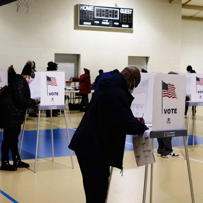 A black man filling out ballot in voting booth on Election Day.
