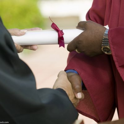 A black man receiving his diploma and giving a handshake.