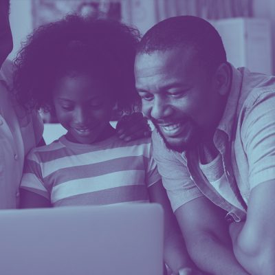 A picture of a black family smiling together as they stare at a computer, with a blue overlay on the photo.