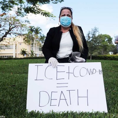 A woman wears a protective face mask and gloves as she protests outside of a U.S. Immigration and Customs Enforcement field office Friday, May 29, 2020, in Plantation, Fla.