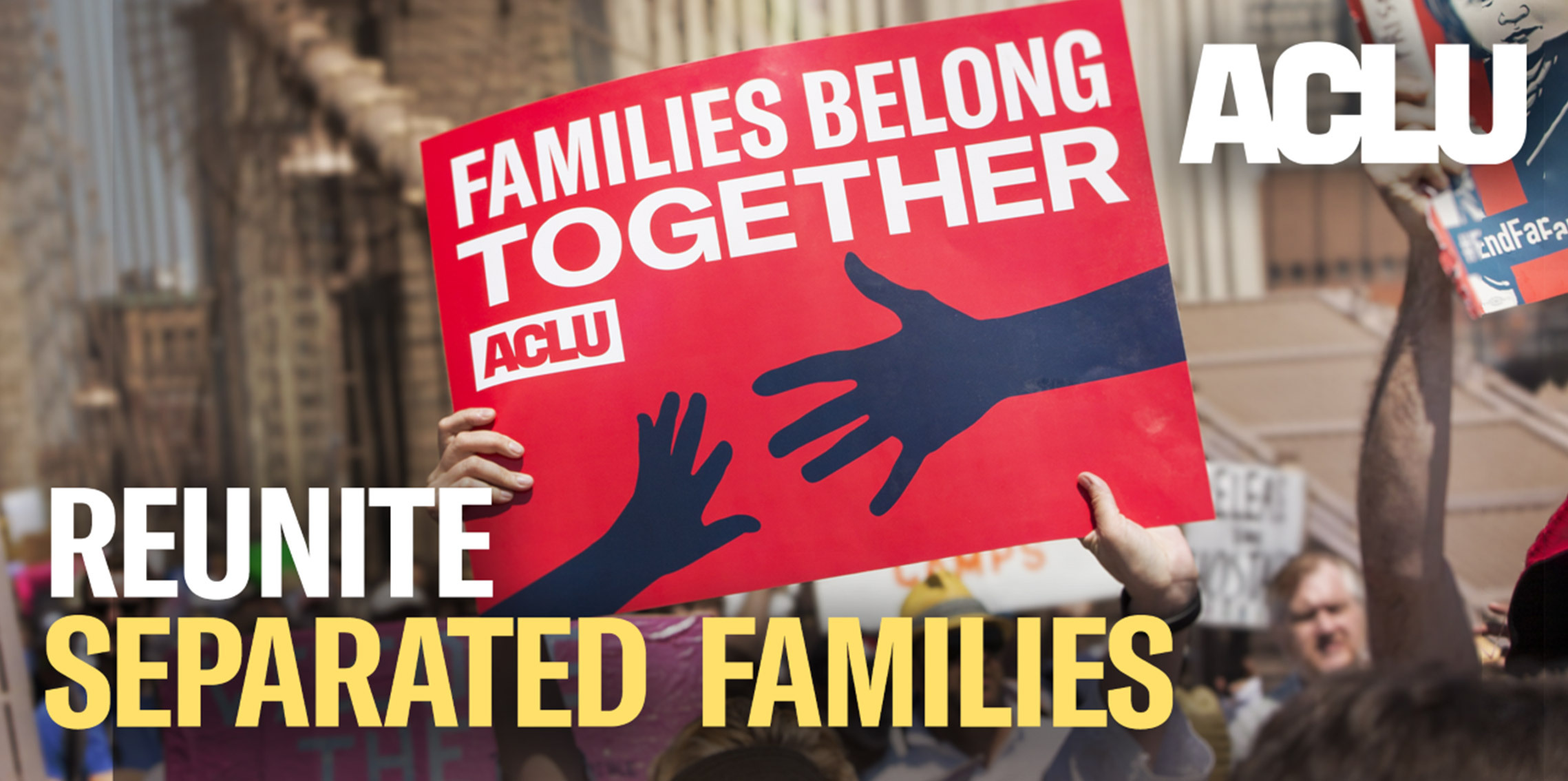 Someone holds an ACLU sign that reads "Families Belong Together"