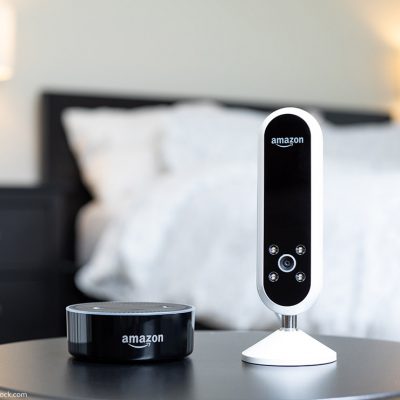 Amazon camera and Amazon Alexa speaker next to each other on a bedside table.