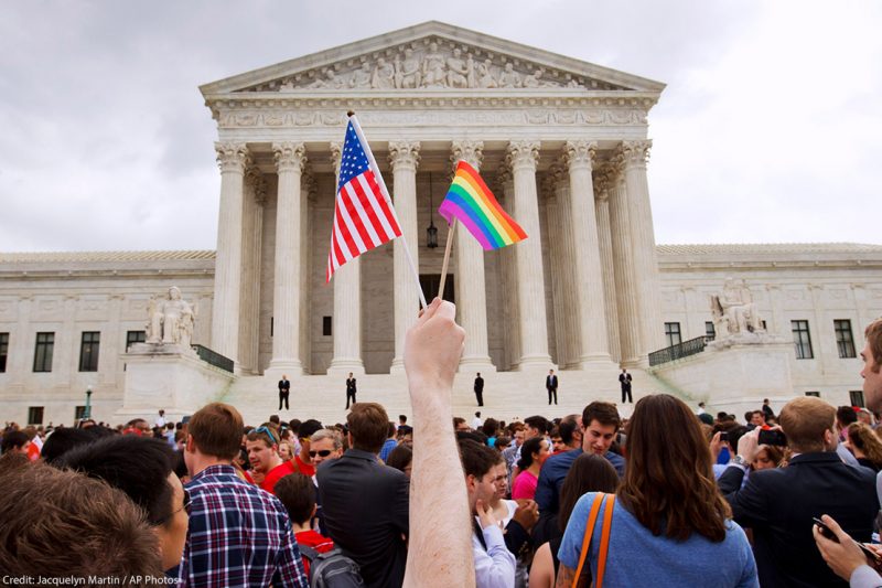 Person holds a mini-American flag and mini-rainbow flag outside of the Supreme Court.