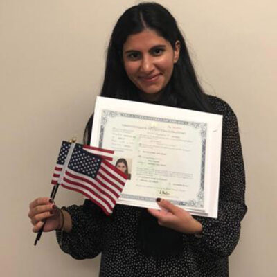Mira Naseer, a diversity visa recipient, holding her naturalization papers and two American flags.