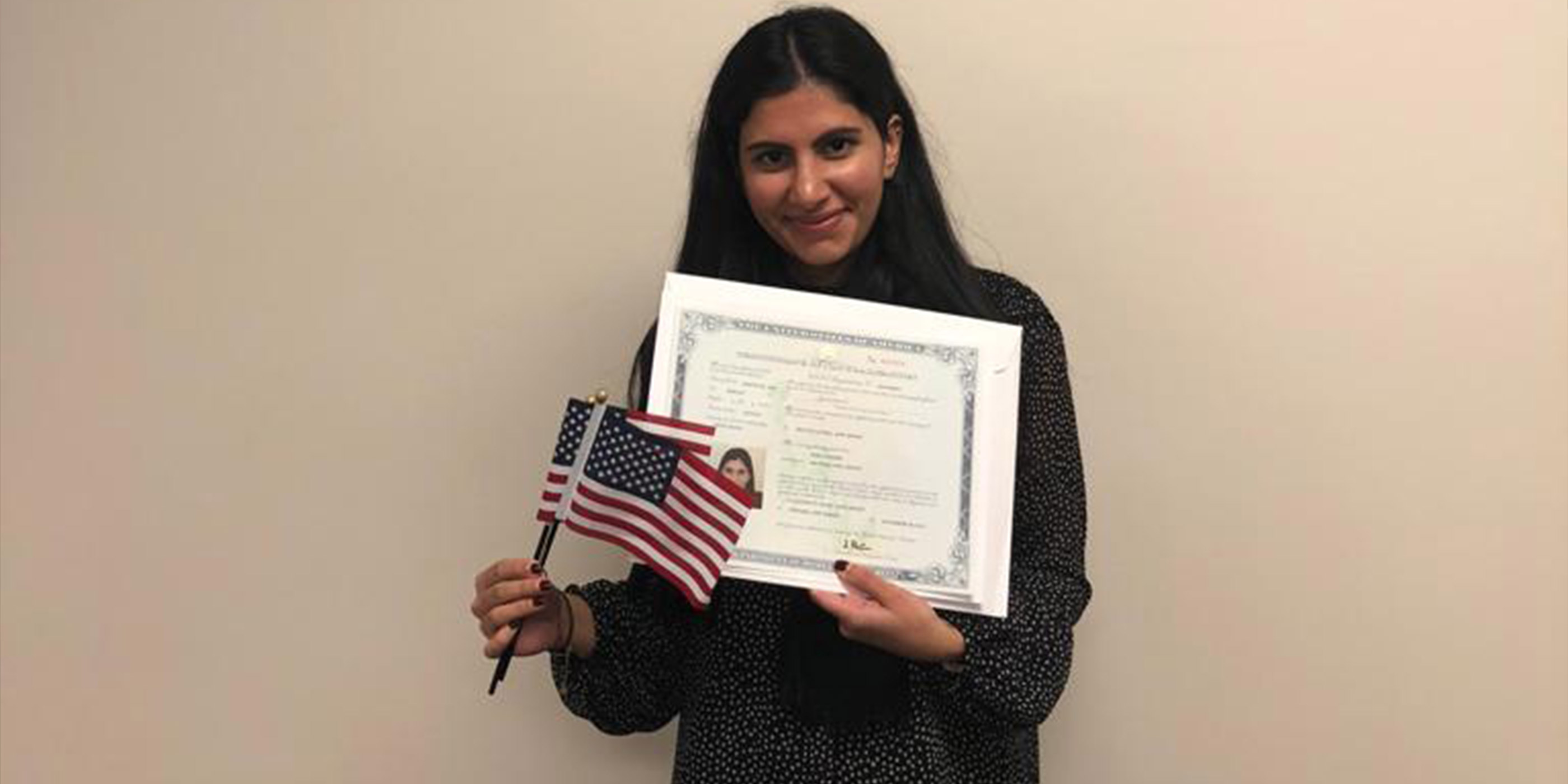 Mira Naseer, a diversity visa recipient, holding her naturalization papers and two American flags.