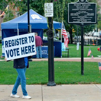 Person holds sign that reads "register to vote here" near a voter registration booth on a Pennsylvania street