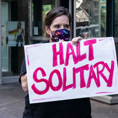 Woman holds sign that reads "halt solitary" as demand to end solitary confinement in prisons