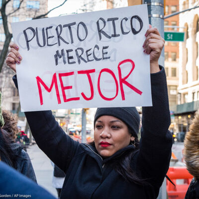 Protestor holds sign that reads "Puerto Rico deserves better" in Spanish
