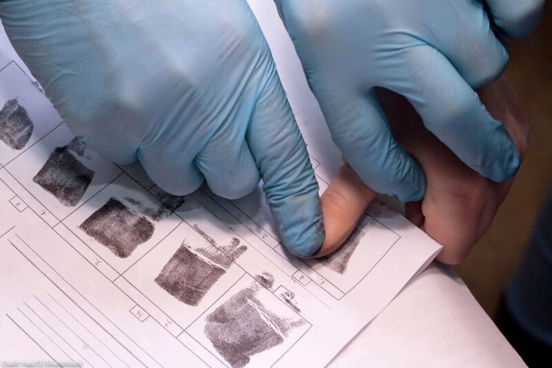 crime investigator wearing gloves fingerprinting person