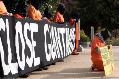 Demonstrators dressed like Guantanamo Bay detainees, hold a banner asking to close Guantanamo.