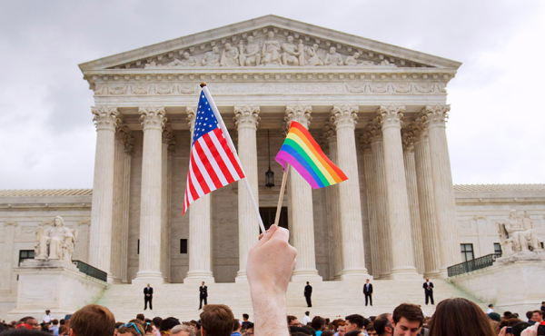a hand holding an American flag and a rainbow flag in front of the supreme court building