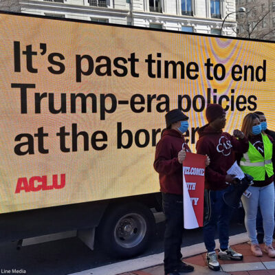 Demonstrators standing in front of a mobile billboard that says, “It’s past time to end Trump-era policies at the border.”