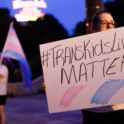 A transgender rights advocate holds a sign saying #TransKidsLivesMatter.