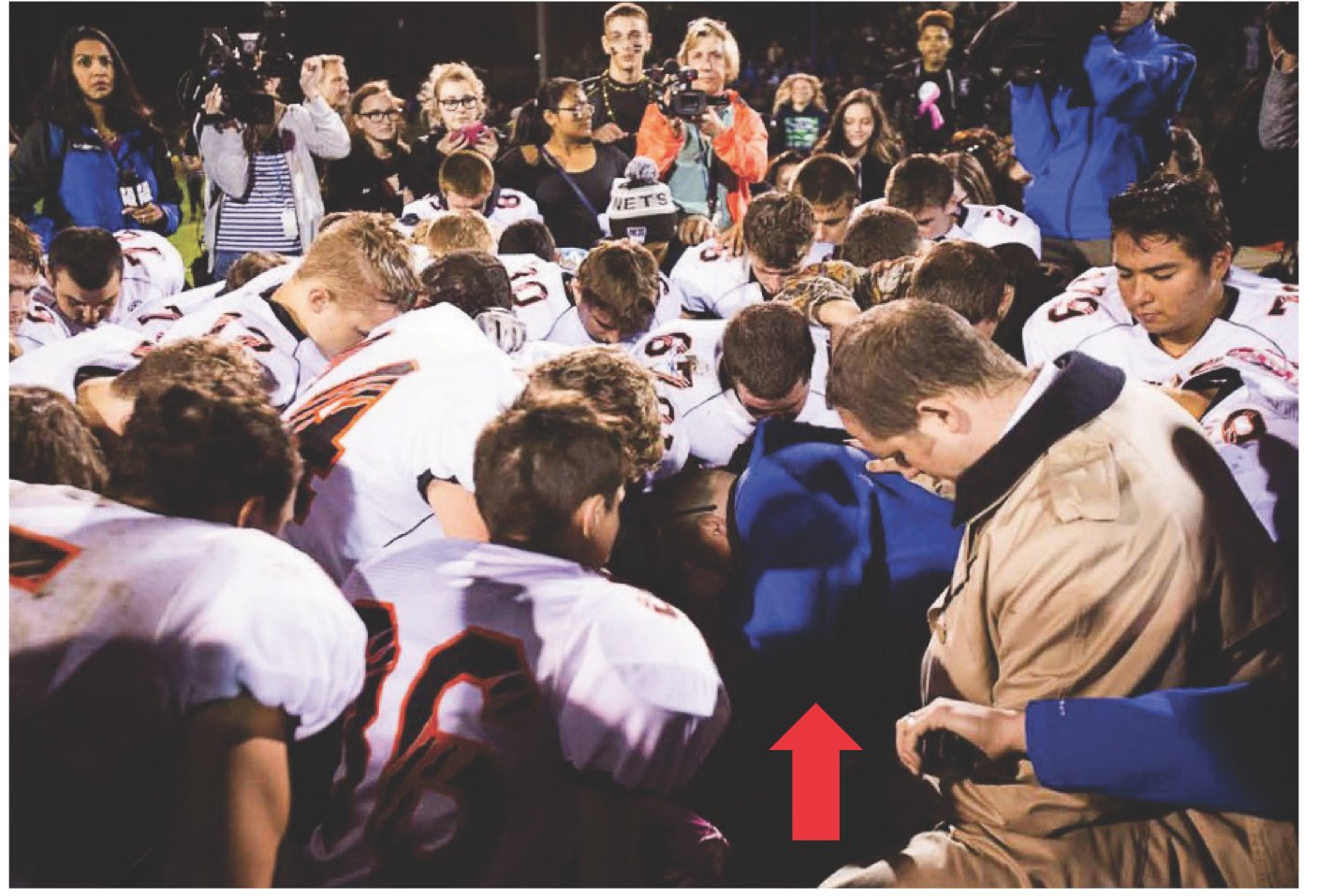 Students being led in prayer by their coach at a Bremerton School District high school. A red arrow is juxtaposed on the image pointing to the coach.