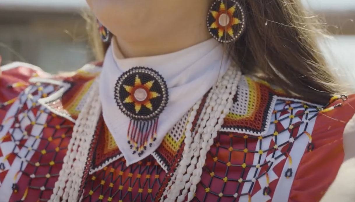 A student wears traditional tribal regalia including a beaded broach and earrings.