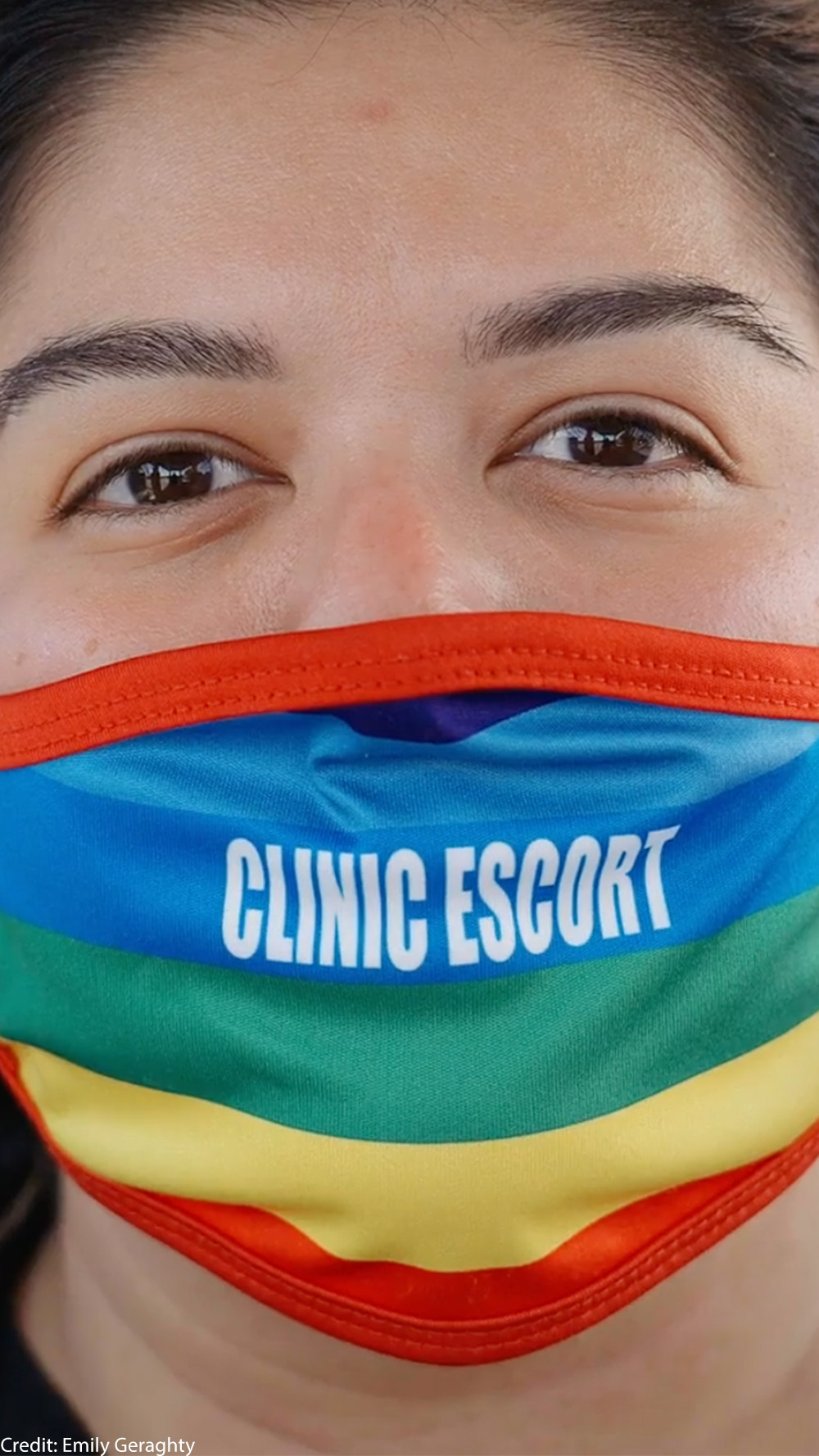 A close-up of Mariceli Alegria who's wearing a rainbow facemask with the printed words "Clinic Escort".