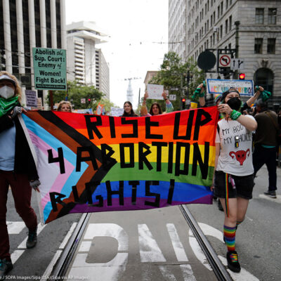 People holding a rainbow flag banner reading "Rise Up 4 Abortion Rights" while marching at the 2022 San Francisco Pride parade of 2022.