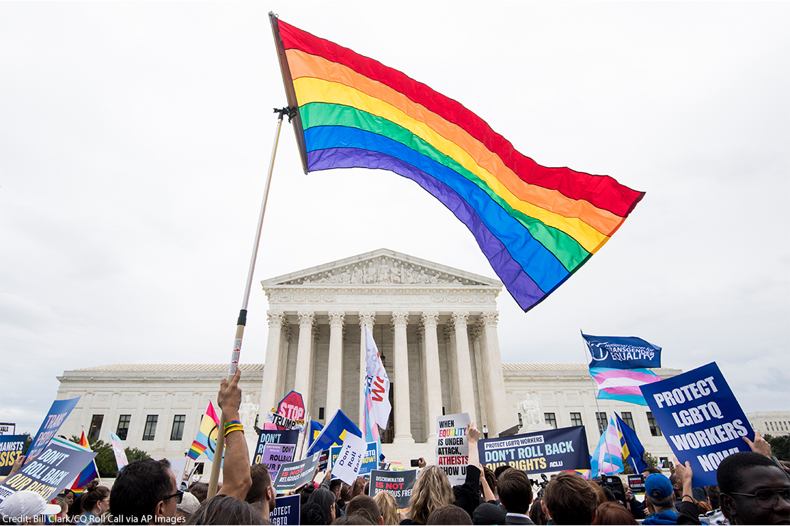 Rallying against transgender discrimination, protestors carry a rainbow flag and signs in front of the Supreme Court.