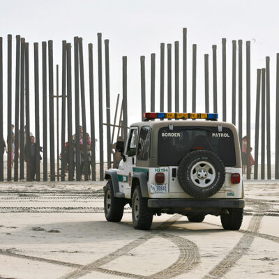 A U.S. Border Patrol vehicle sits parked in front of a crowd of people peering through the U.S.-Mexico border fence in San Diego.