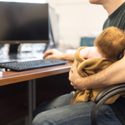 A man holding a baby while on a computer.