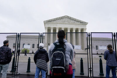Standing beyond security gates that have signs reading "Area Closed", several people stare at the Supreme Court building.