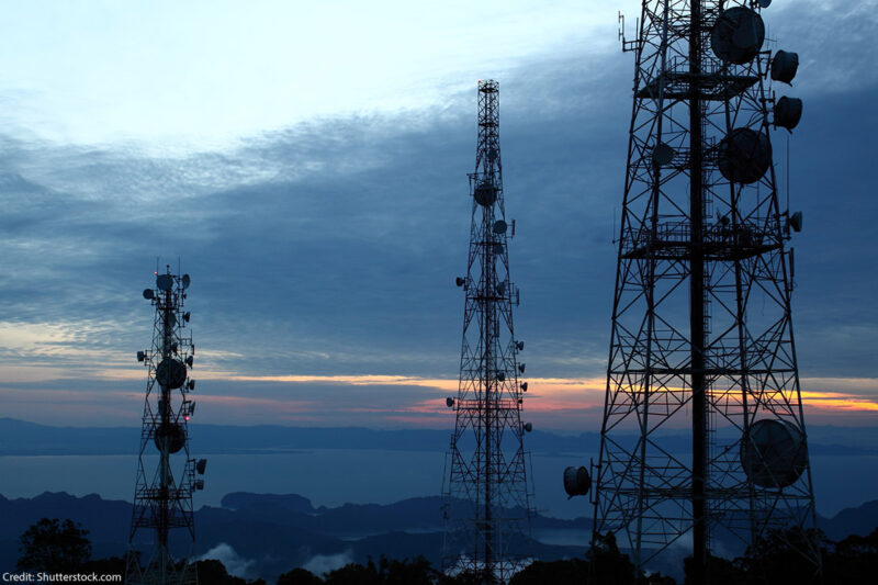 A photo of three cell phone towers in front of a sunset.