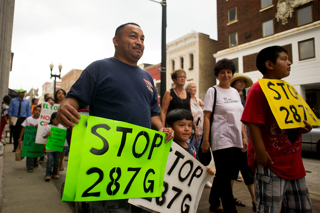 Demonstrators marching in protest against the federal immigration program 287(g). Leading the march and holding signs reading "STOP 287G" are a father, his two sons and others trailing behind.
