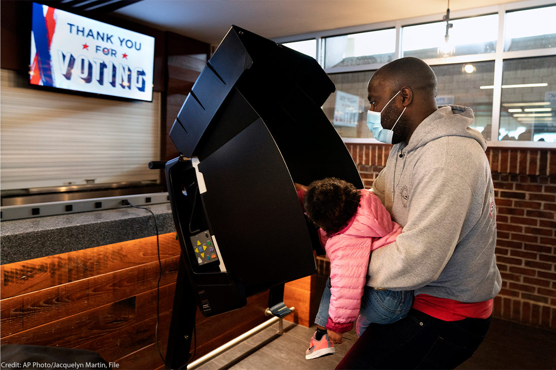 An African-American father has his 2 year-old daughter help him push the button while casting his vote at an early voting center at Nationals Park in Washington.