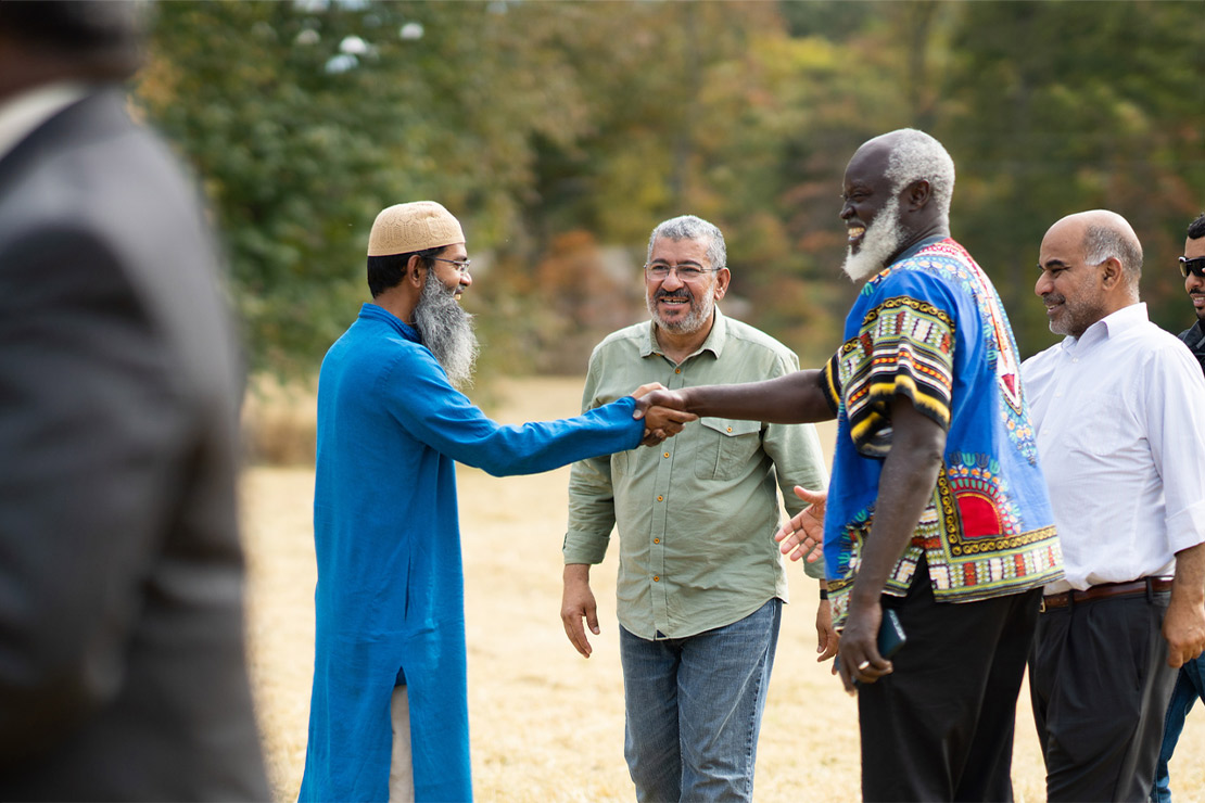 Two smiling men (members of the Abraham House of God, the first mosque in DeSoto County Mississippi) shake hands as they greet each other while another smiling man looks on.