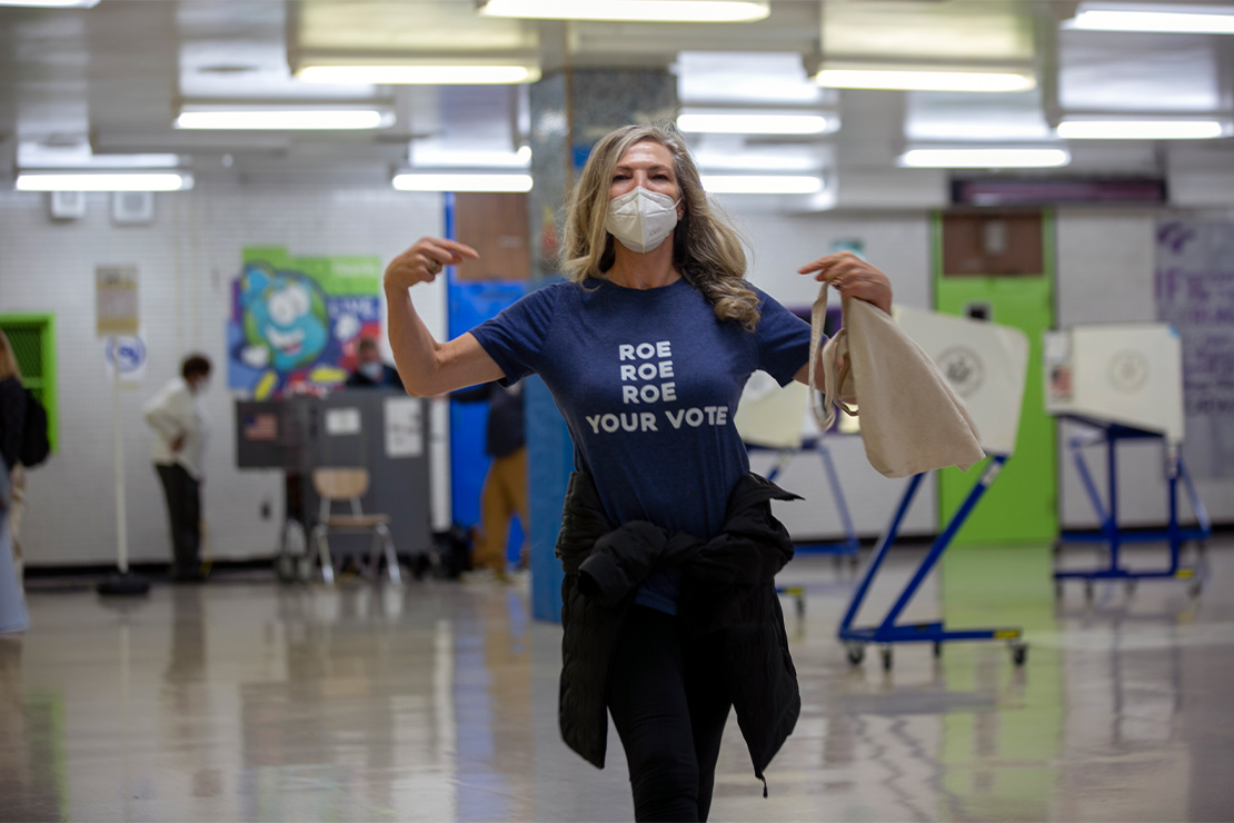 A woman pointing to her t-shirt reading "Roe Roe Roe Your Vote" at an early voting polling site in New York City.