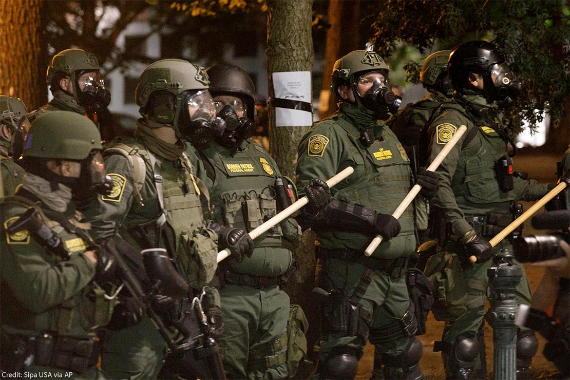 Border Patrol agents in green uniforms with wooden batons stand in a line as protesters rallied outside the Hatfield Federal Courthouse in Portland, Oregon on the night of July 29, 2020.
