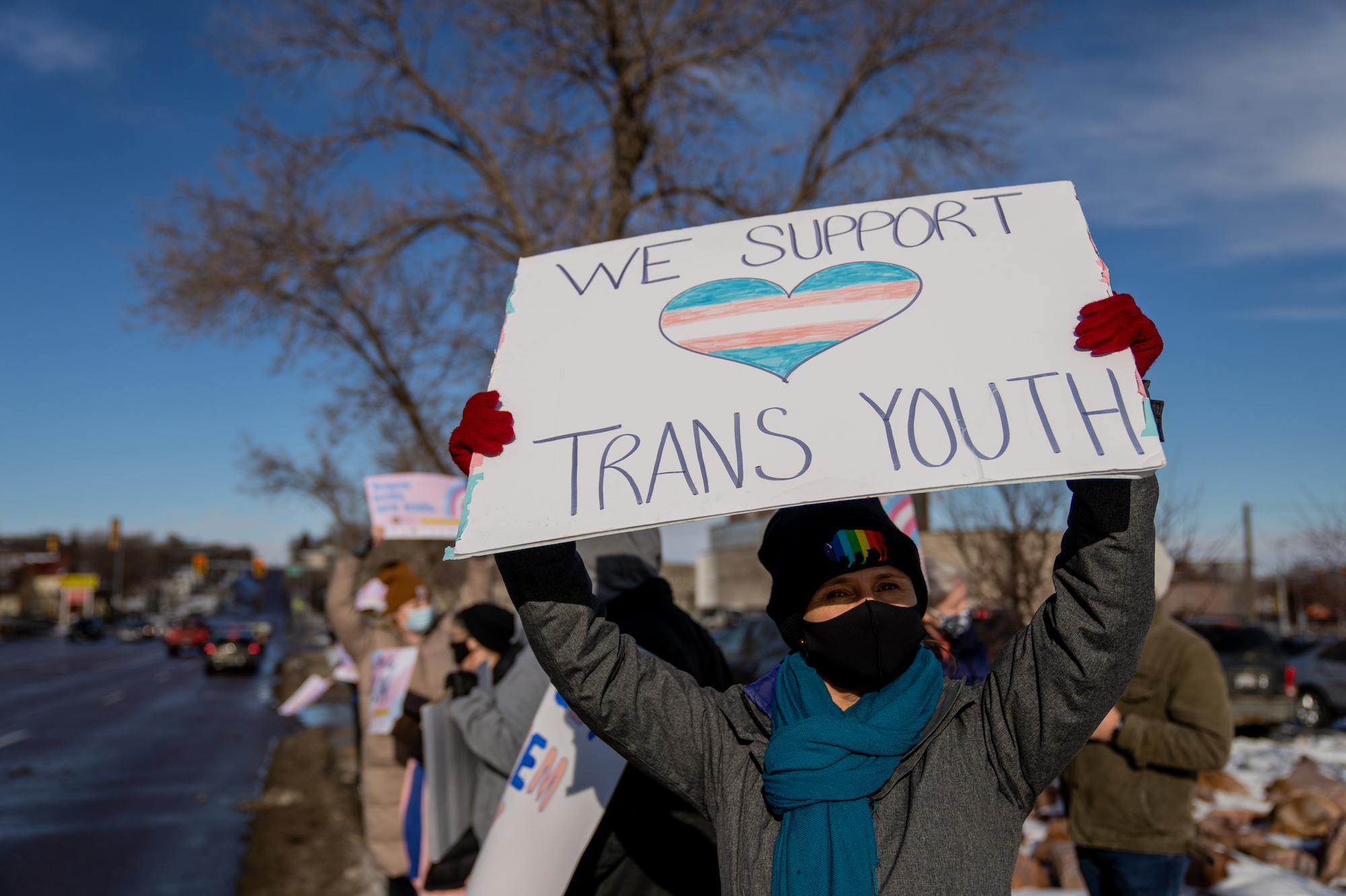 A person holding a sign reading "We Support Trans Youth."