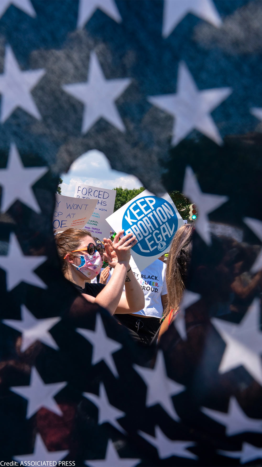 Abortion rights activists are seen through a hole in an American flag as they protest outside the Supreme Court in Washington, Saturday, June 25, 2022.