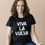 Dr. Jennifer Lincoln is a white woman with brown hair. She is against a beige backdrop wearing a black tshirt that says "viva la vulva" in white letters.