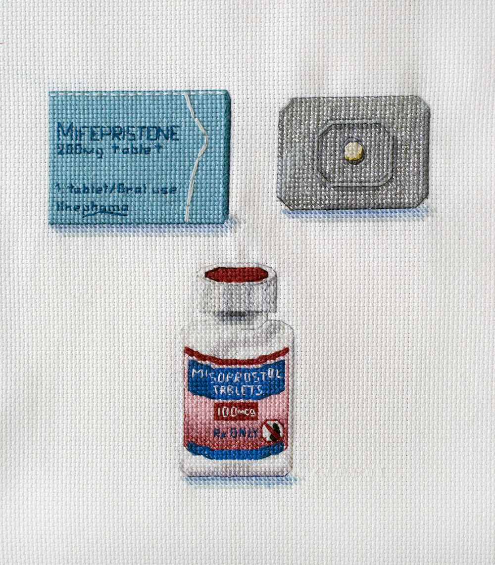 An embroidered art piece by Katrina Majkut, which features two pills used in medication abortion, Mifepristone and Misoprostol.