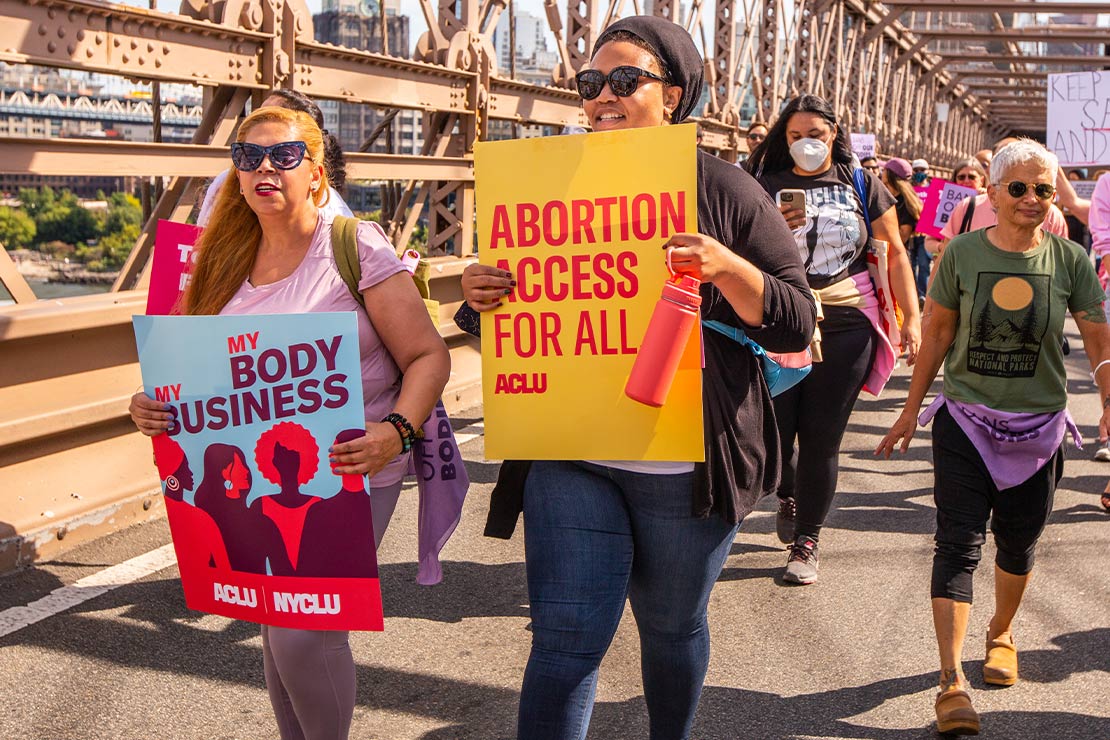 ACLU supporters crossing the Brooklyn Bridge, holding signs reading Abortion Access for All.