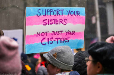 A demonstration sign reading "Support Your Sisters, Not Just Your Cis-ters."