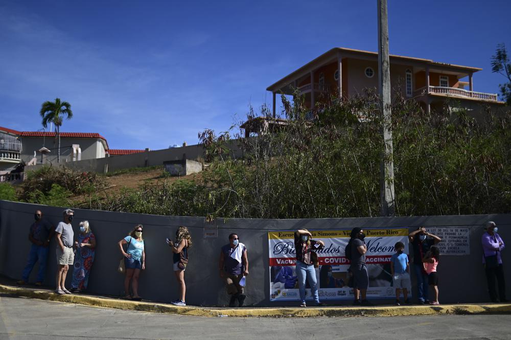People stand in line outside a Puerto Rico elementary school waiting to be inoculated against COVID-19 as part of a mass vaccination campaign on the Island.