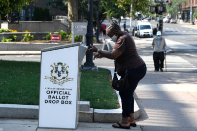An Afrian-American woman drops a ballot into a State of Connecticut Official Ballot Drop Box outside Hartford City Hall.