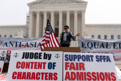 A speaker in front of protest signs regarding fair college admissions in front of the Supreme Court.
