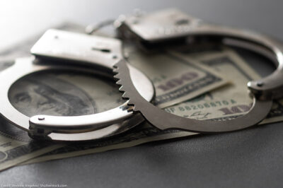 A pair of handcuffs over several 100 dollar bills.