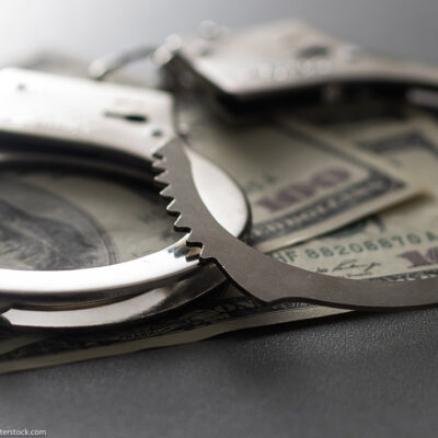A pair of handcuffs over several 100 dollar bills.